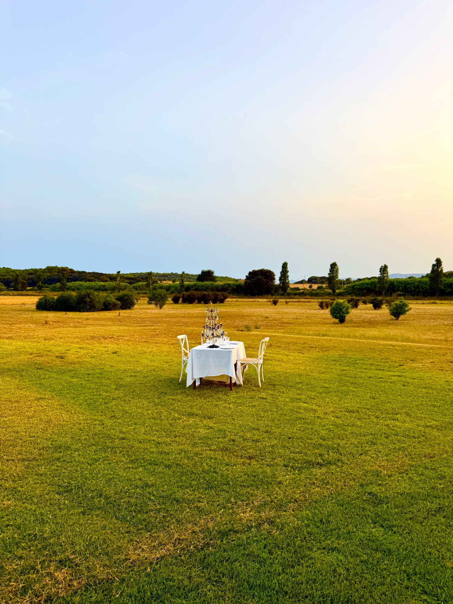 Mesa para dos servida al aire libre en un prado, con candelabro y mantel blanco